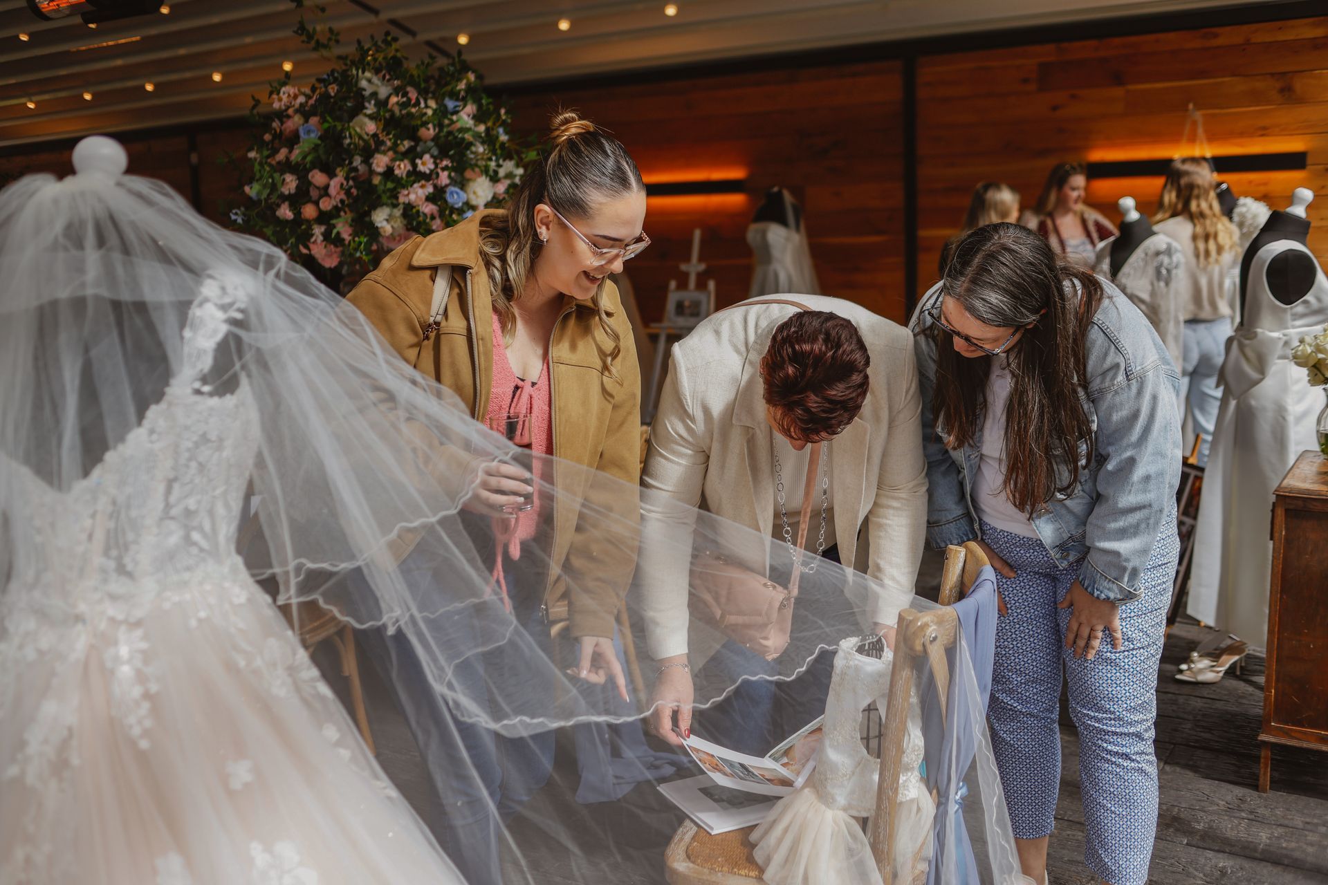 People examining a white bridal gown with a long veil in a boutique.