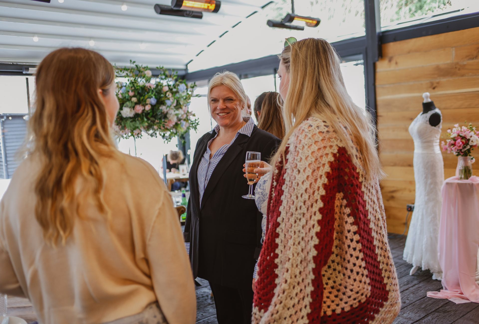 Three people chatting at an outdoor bridal shop display with wedding dresses and hanging flowers.