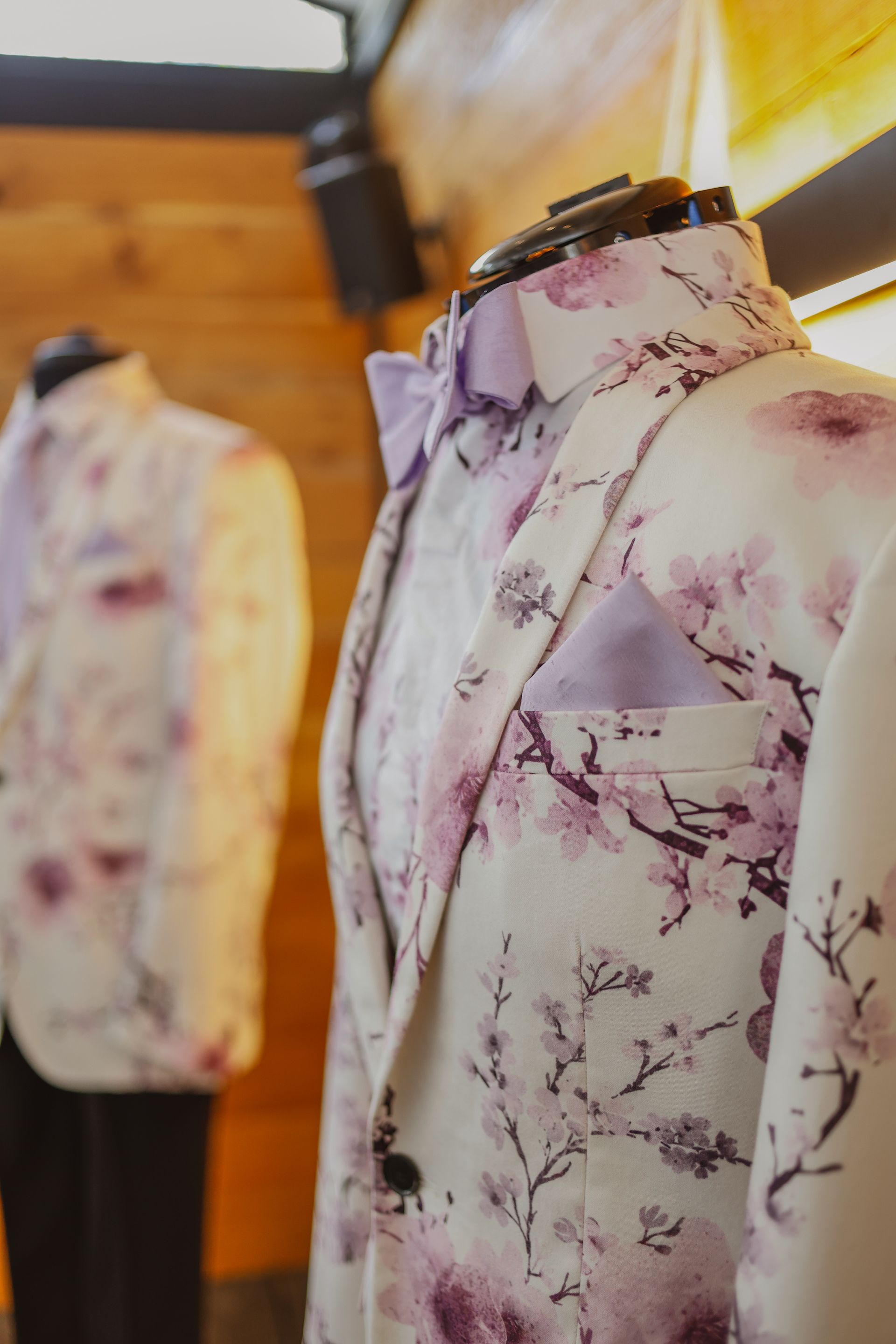 Two floral-patterned blazers on mannequins in a warmly lit clothing store.