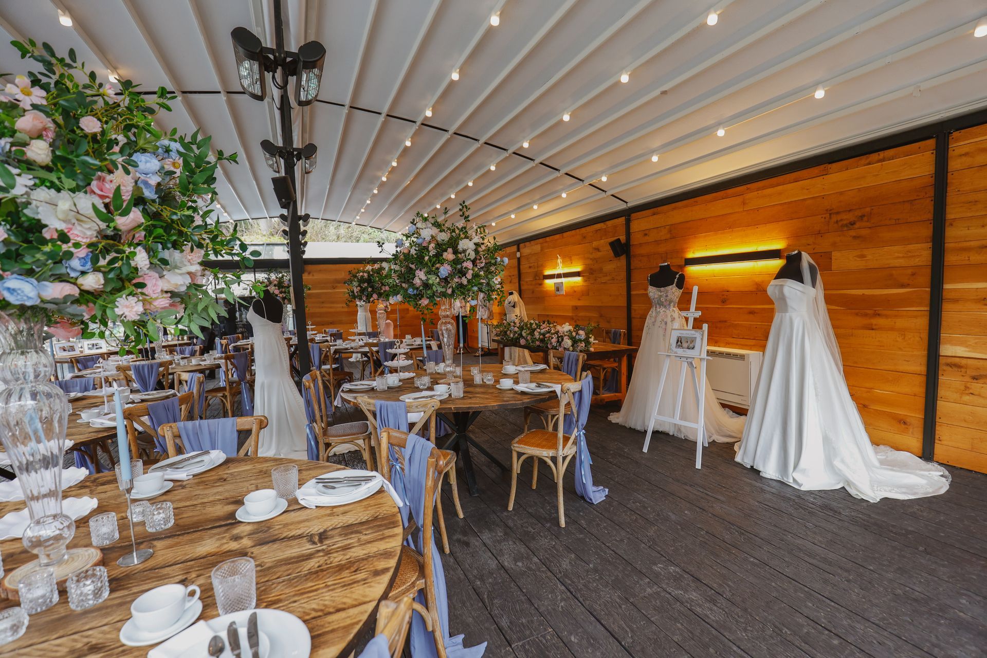 Decorated outdoor wedding reception tent with round tables, white drapes, string lights, and floral arrangements