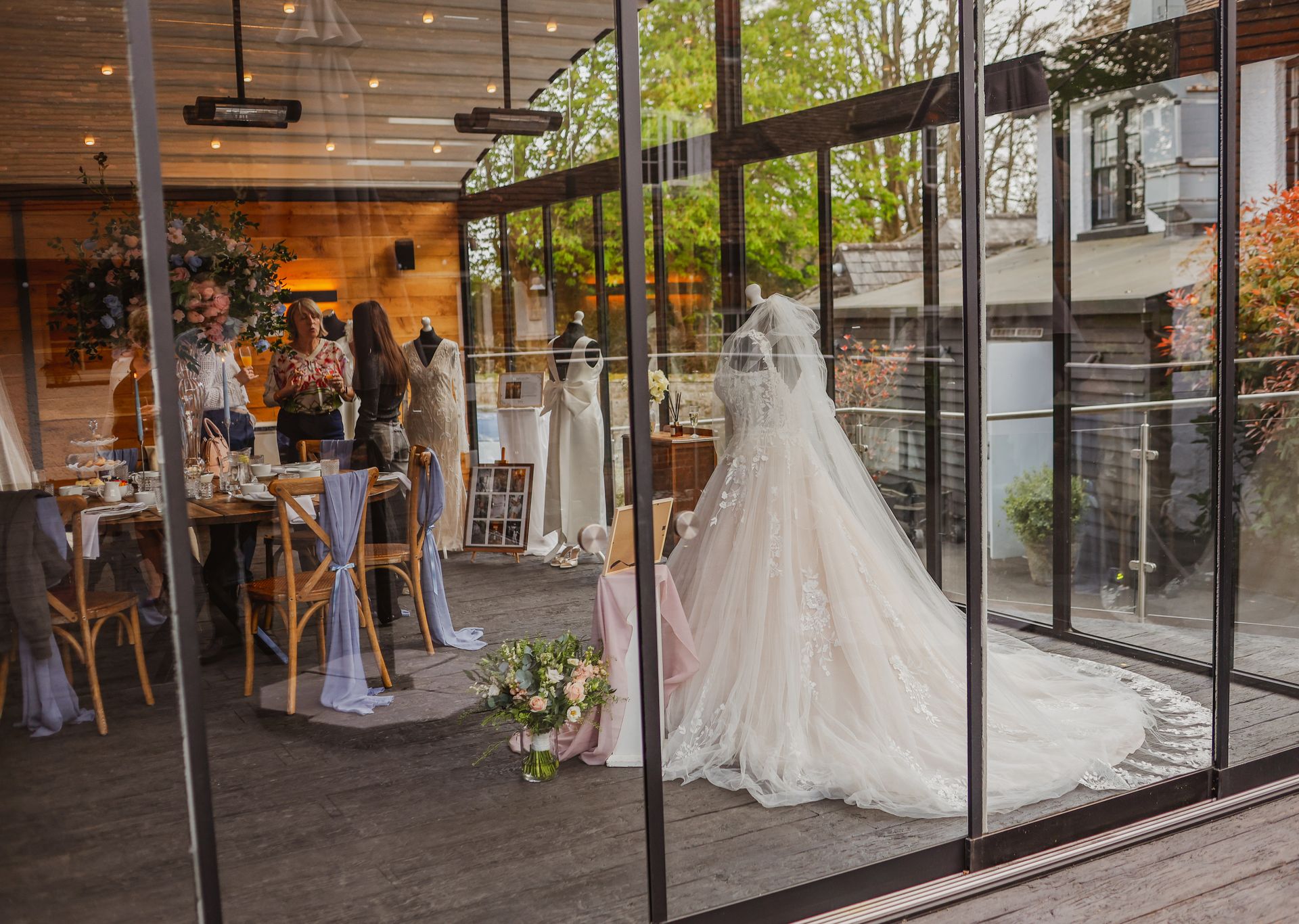 Wedding dress on display in a glass-fronted shop, with guests seated inside the venue.
