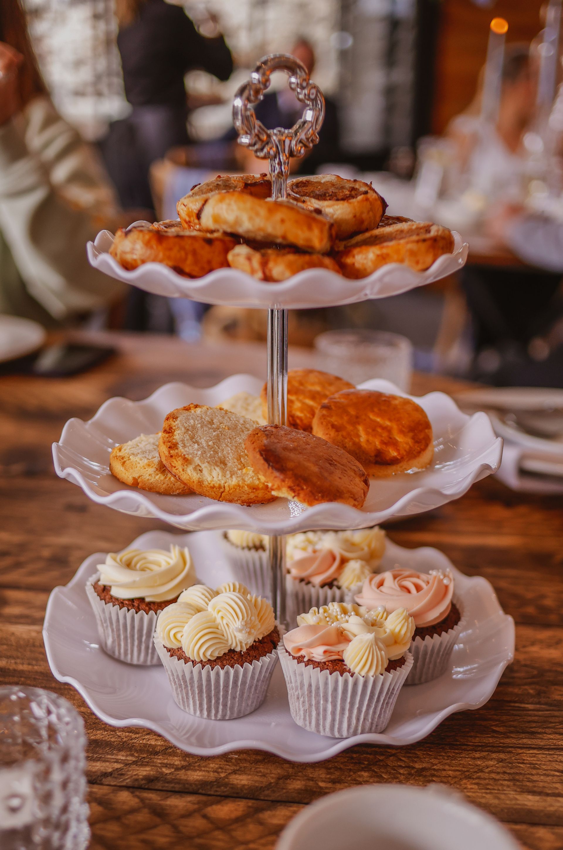 Tiered dessert stand with pastries and frosted cupcakes on a wooden table