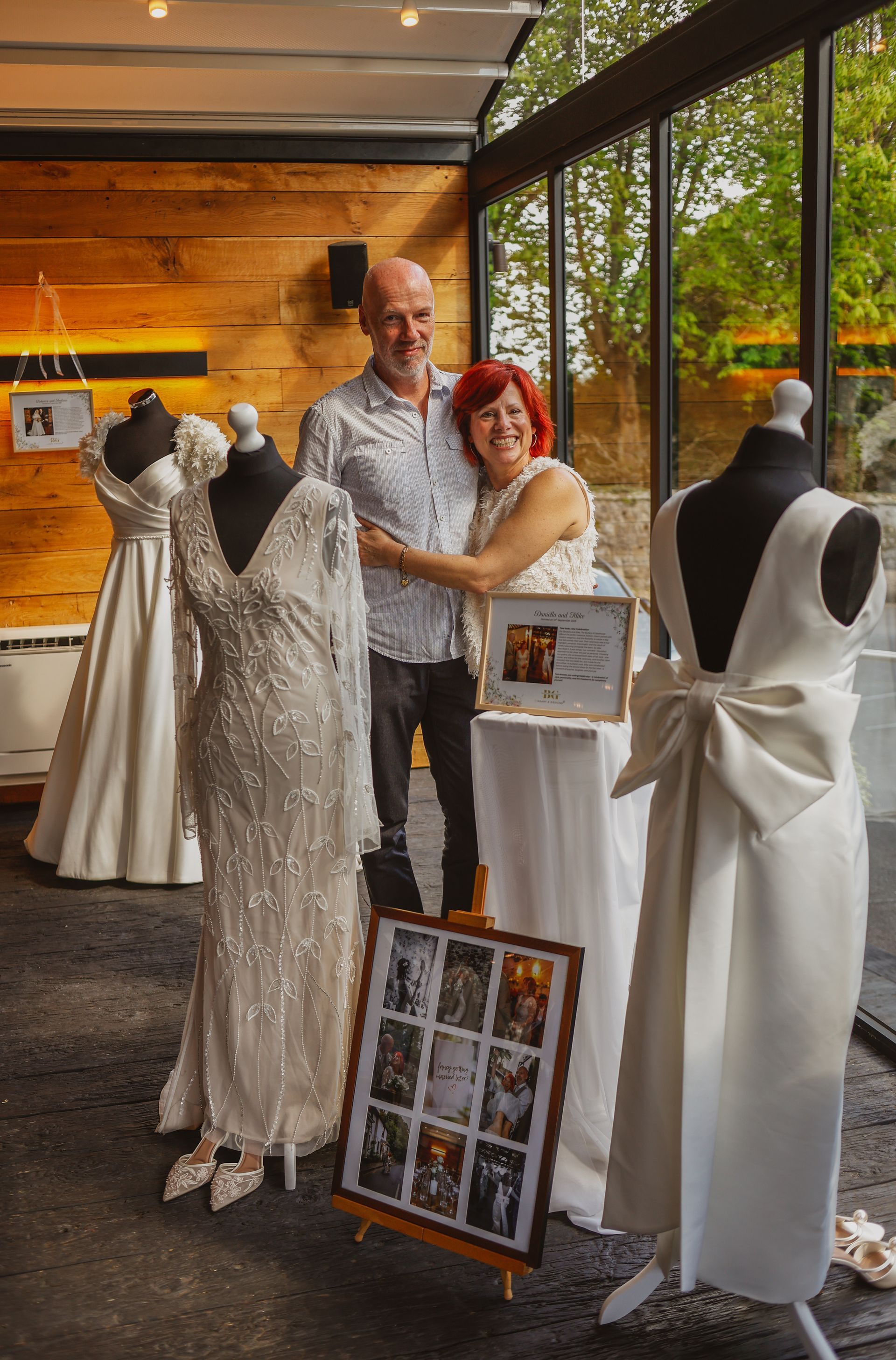 Man and woman posing beside lace mannequins and framed display boards in a boutique showroom