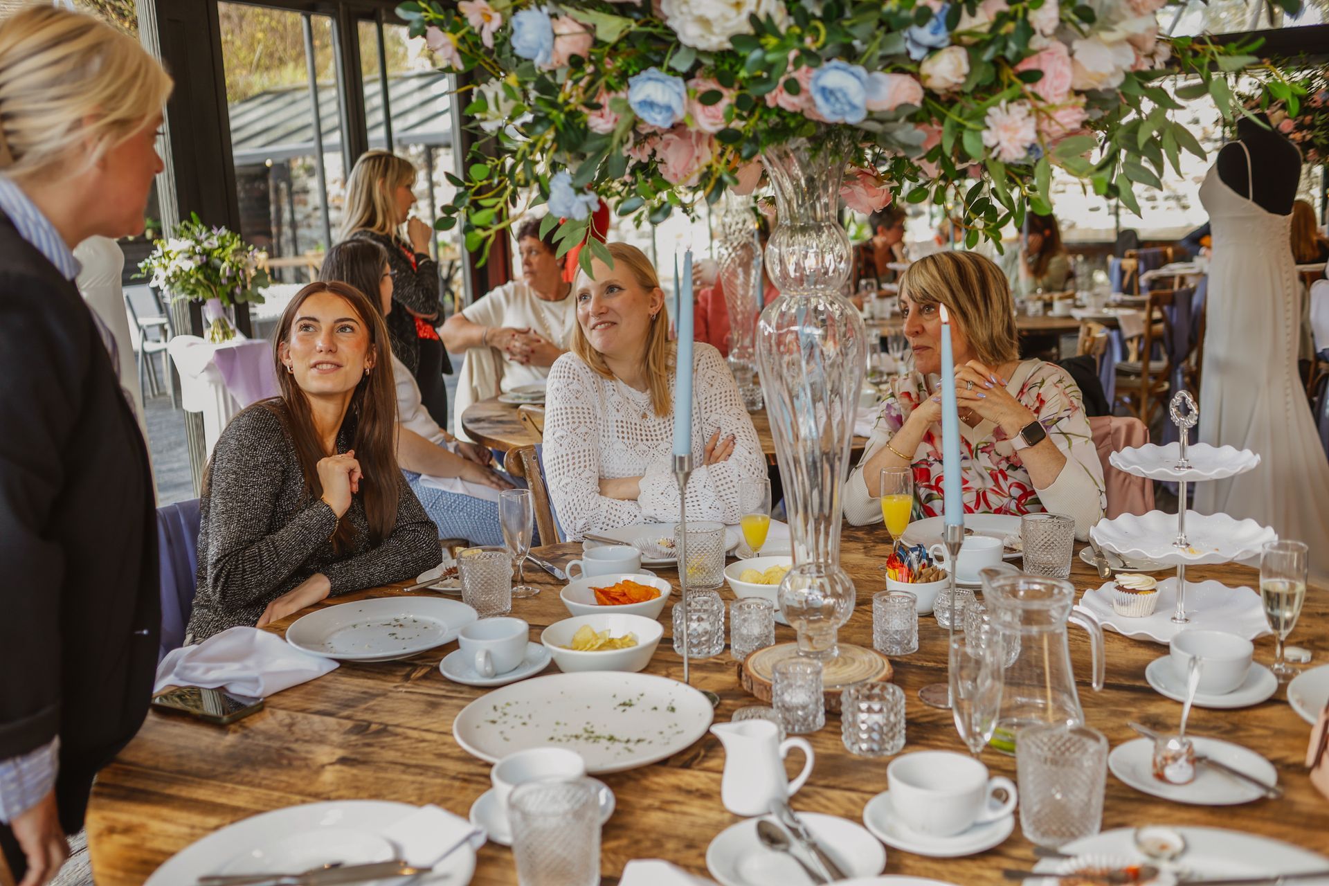Guests seated at a flower-decorated outdoor wedding table, dining and chatting under a canopy.