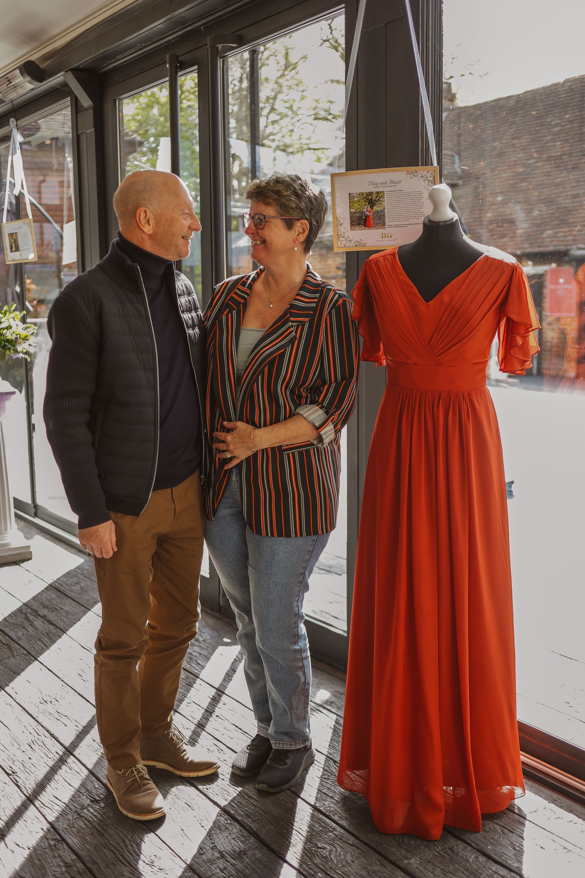 Two people talking beside a mannequin in an orange dress near a shop window.