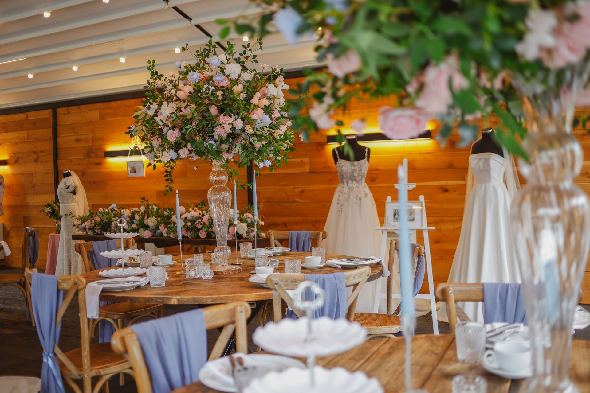 Elegant banquet hall with wooden tables, white chair covers, and pink floral centerpieces under warm lighting