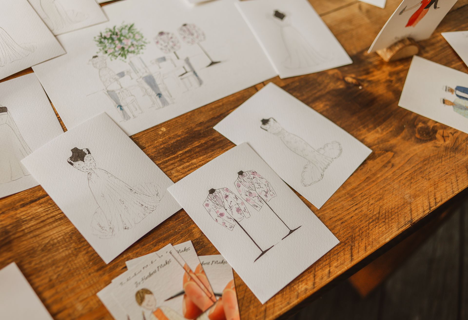 Sketches of dresses and fashion illustrations spread across a wooden table.