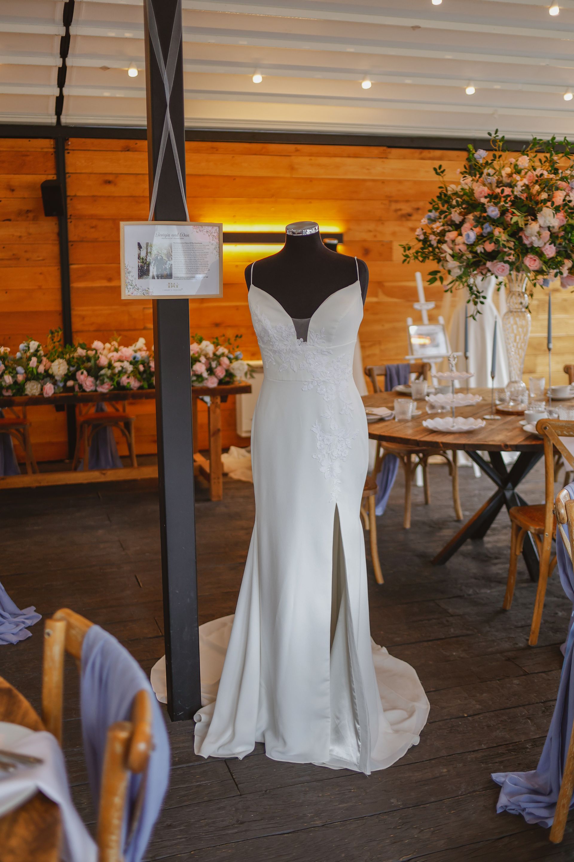 White wedding dress on a mannequin in an indoor reception venue with tables and floral decor