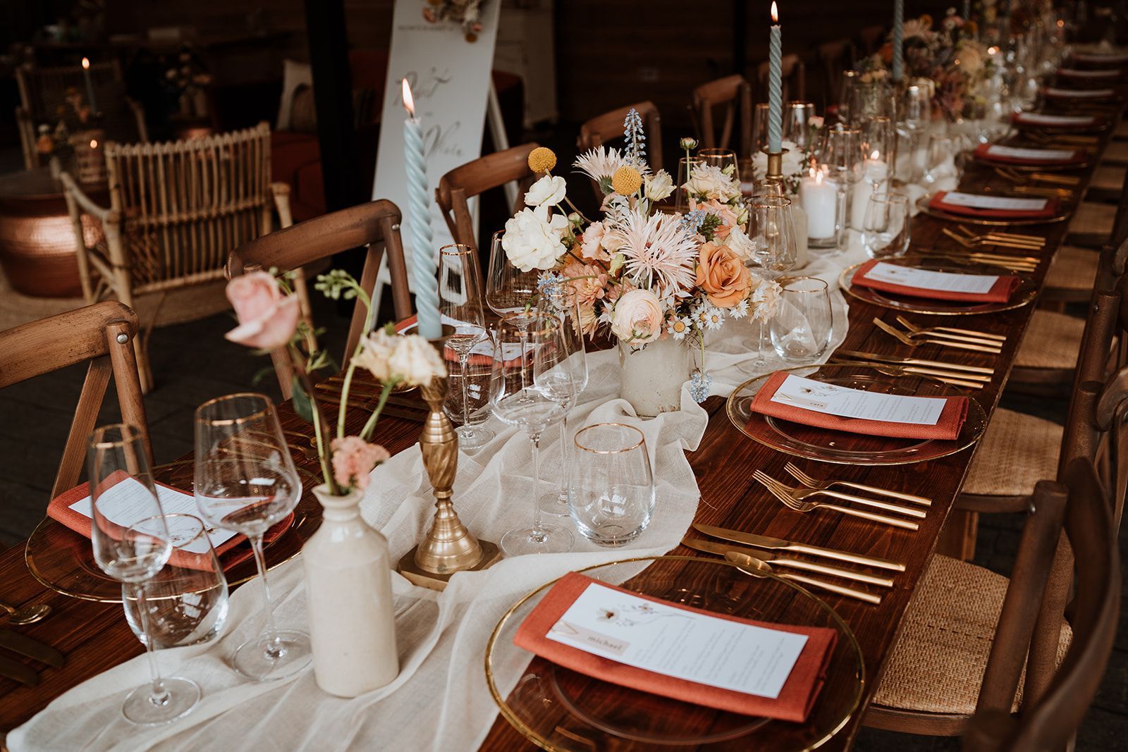 Elegant long dining table set with candles, flowers, wine glasses, and red menus in a rustic venue