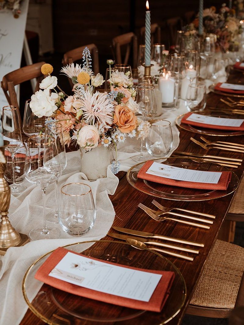Elegant long dining table set with red napkins, glassware, and pastel floral centerpieces