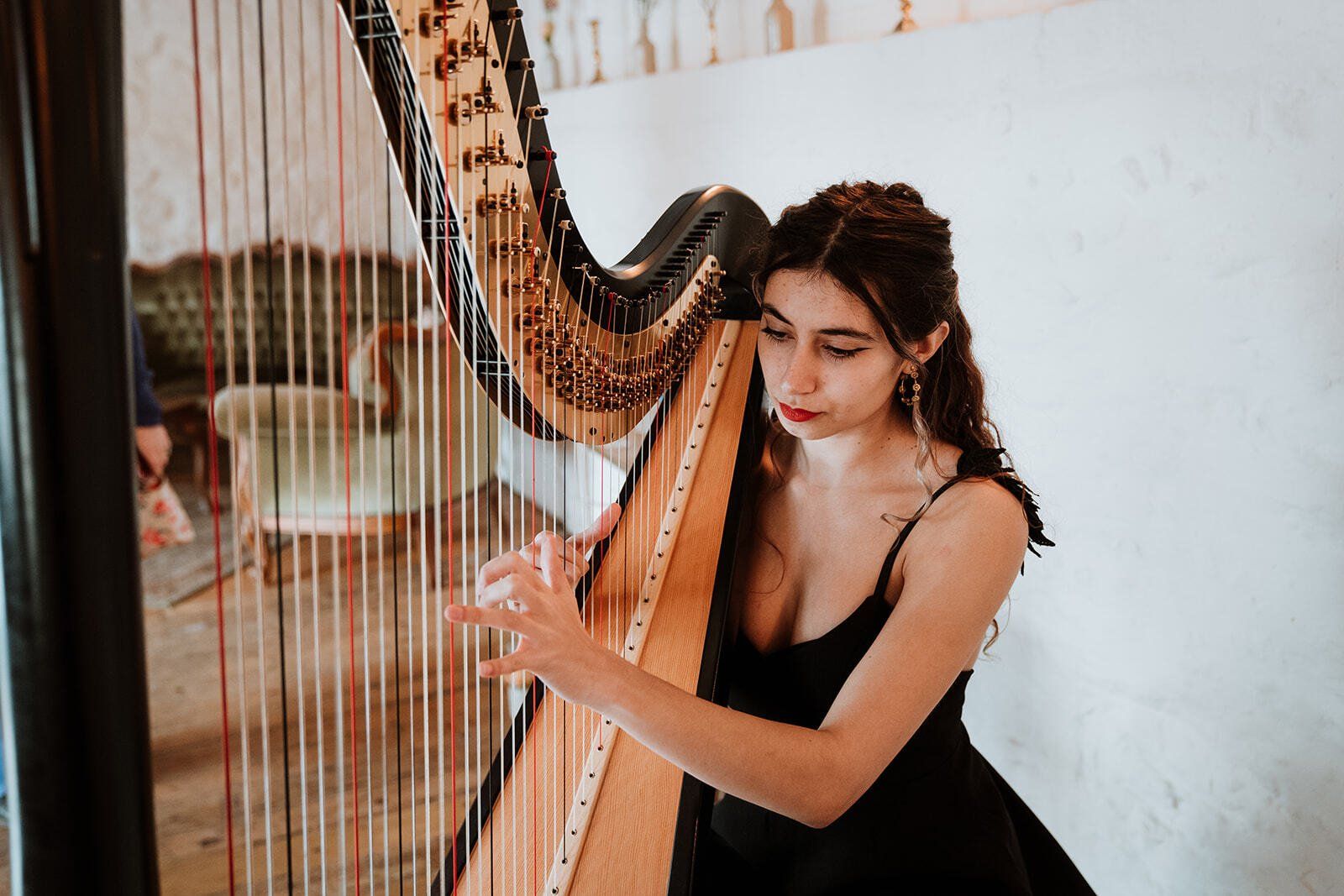 Woman playing a harp indoors, with a focused expression and a black dress