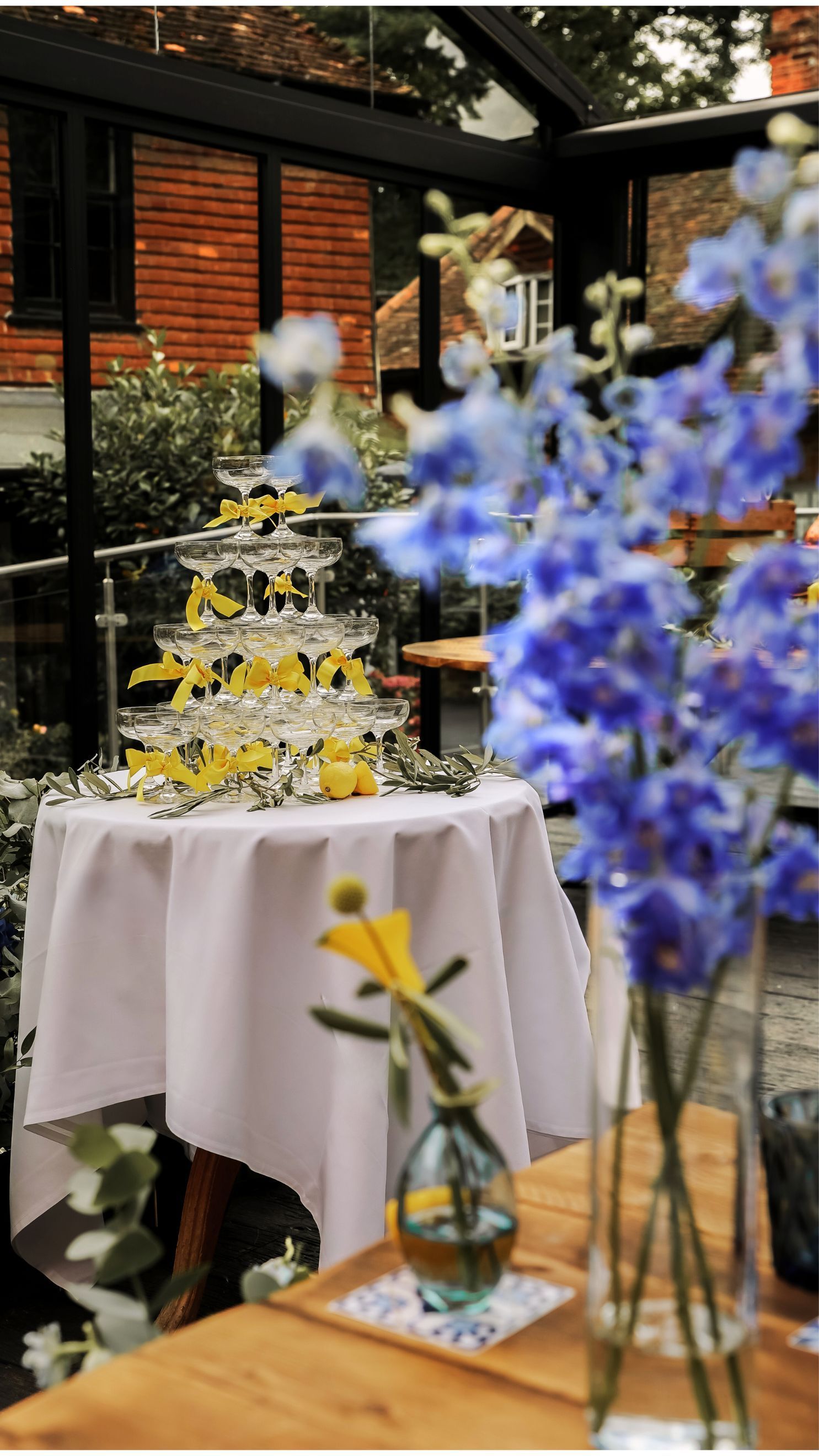Wedding cake on a white table with blue and yellow flowers in a garden setting