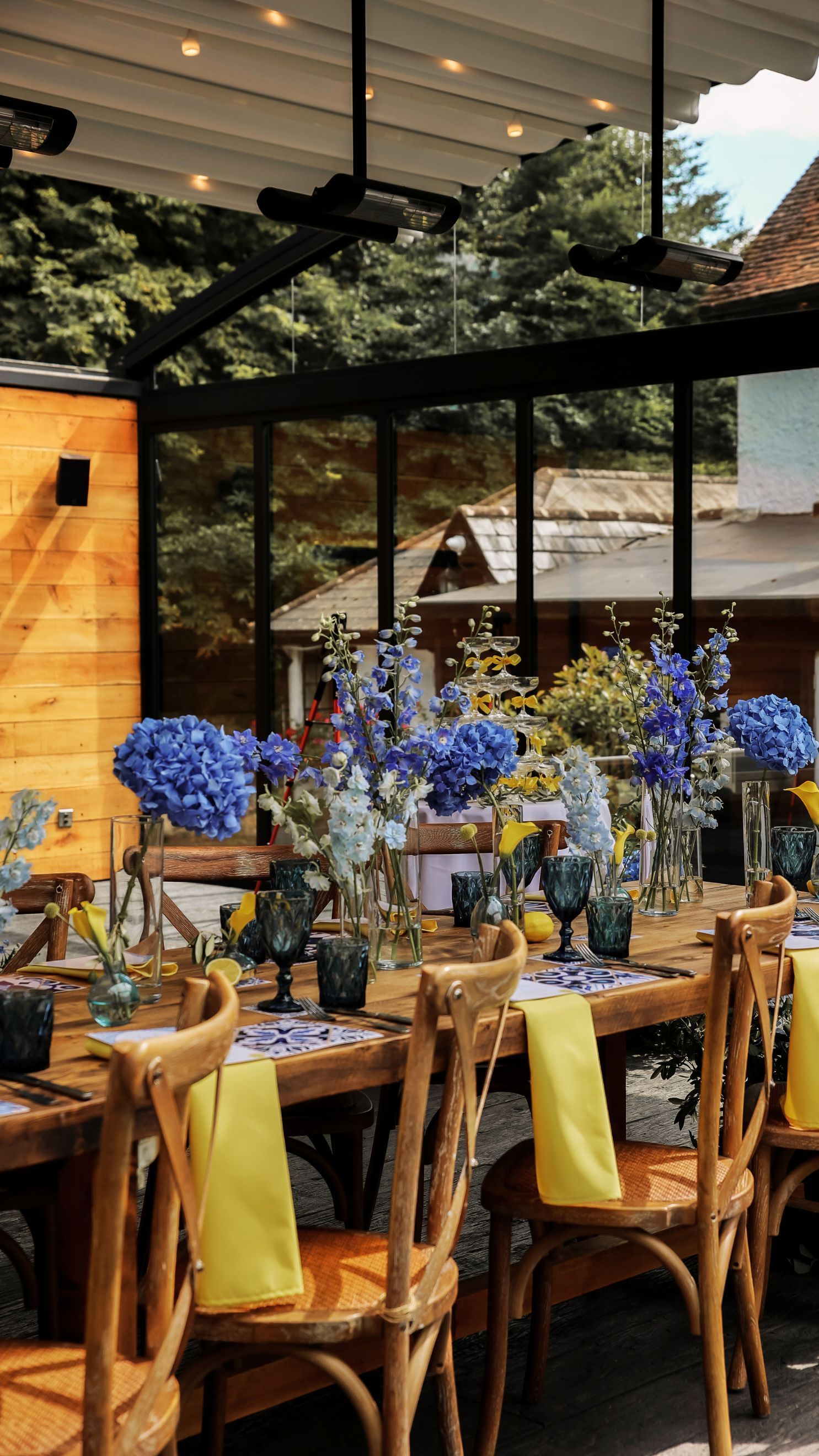 Elegant dining table with blue hydrangeas, wooden chairs, and a glass-roofed restaurant setting