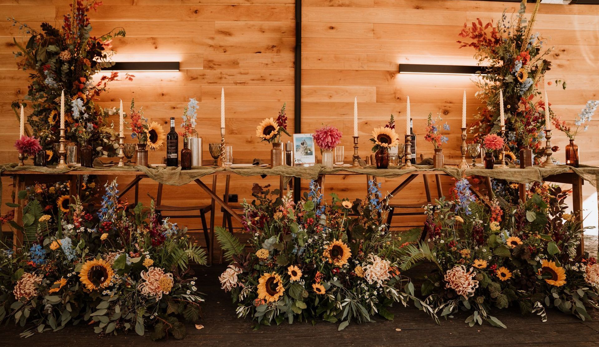 Floral wedding ceremony backdrop with candles, sunflowers, and greenery against a wooden wall