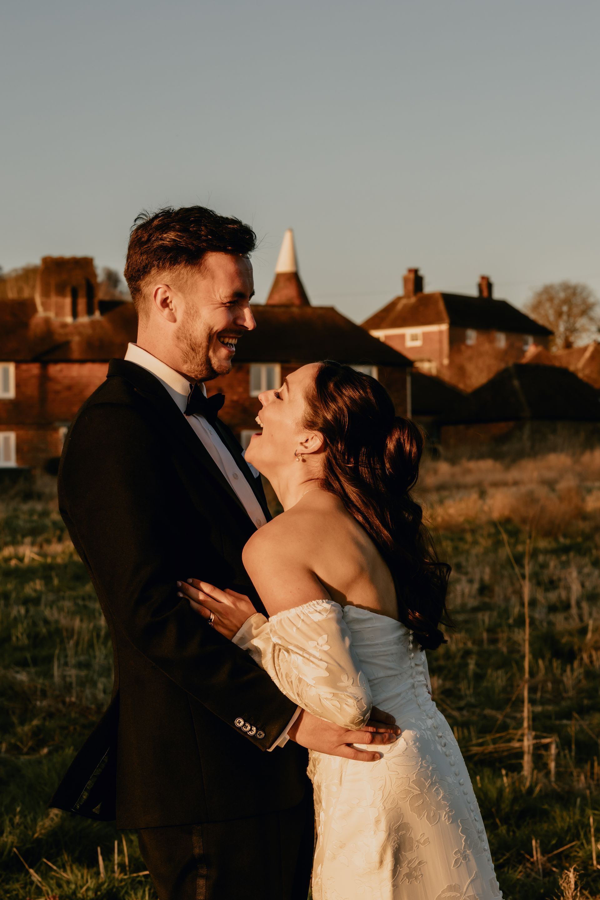 Couple embracing outdoors at sunset, with a village in the background.