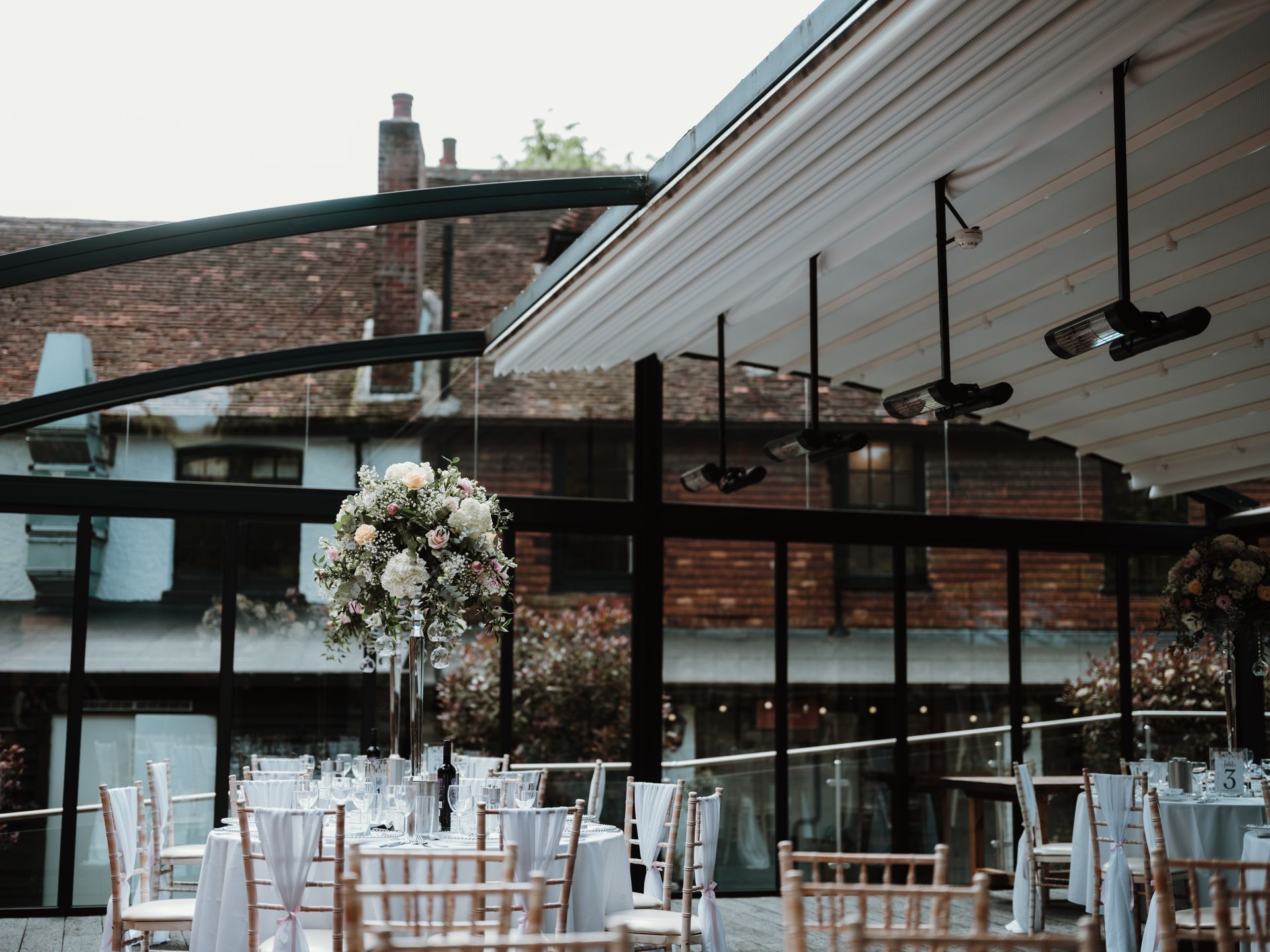 Outdoor wedding reception setup with white chairs, floral centerpieces, and string lights under a covered patio