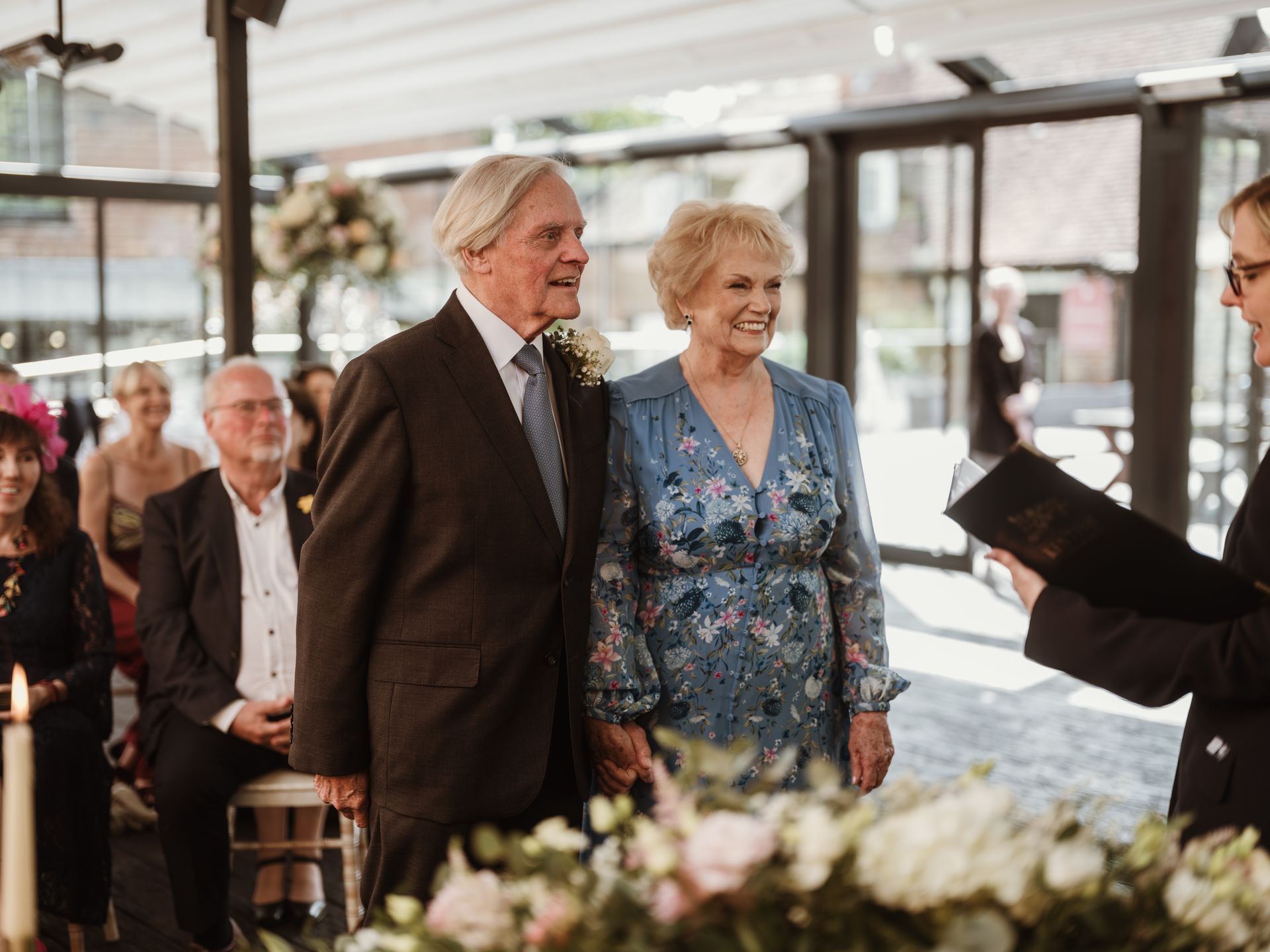 Couple standing together at a wedding ceremony, smiling beside floral arrangements