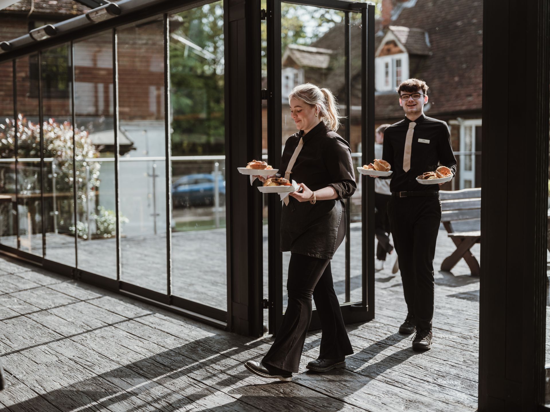 Two people walking with plates through a sunlit glass doorway in a modern building