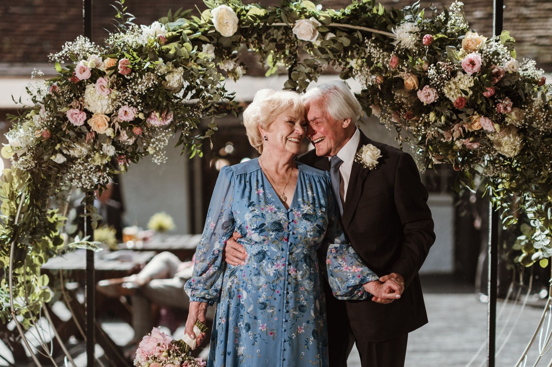 Couple standing under a floral arch, smiling and holding hands at an elegant outdoor ceremony