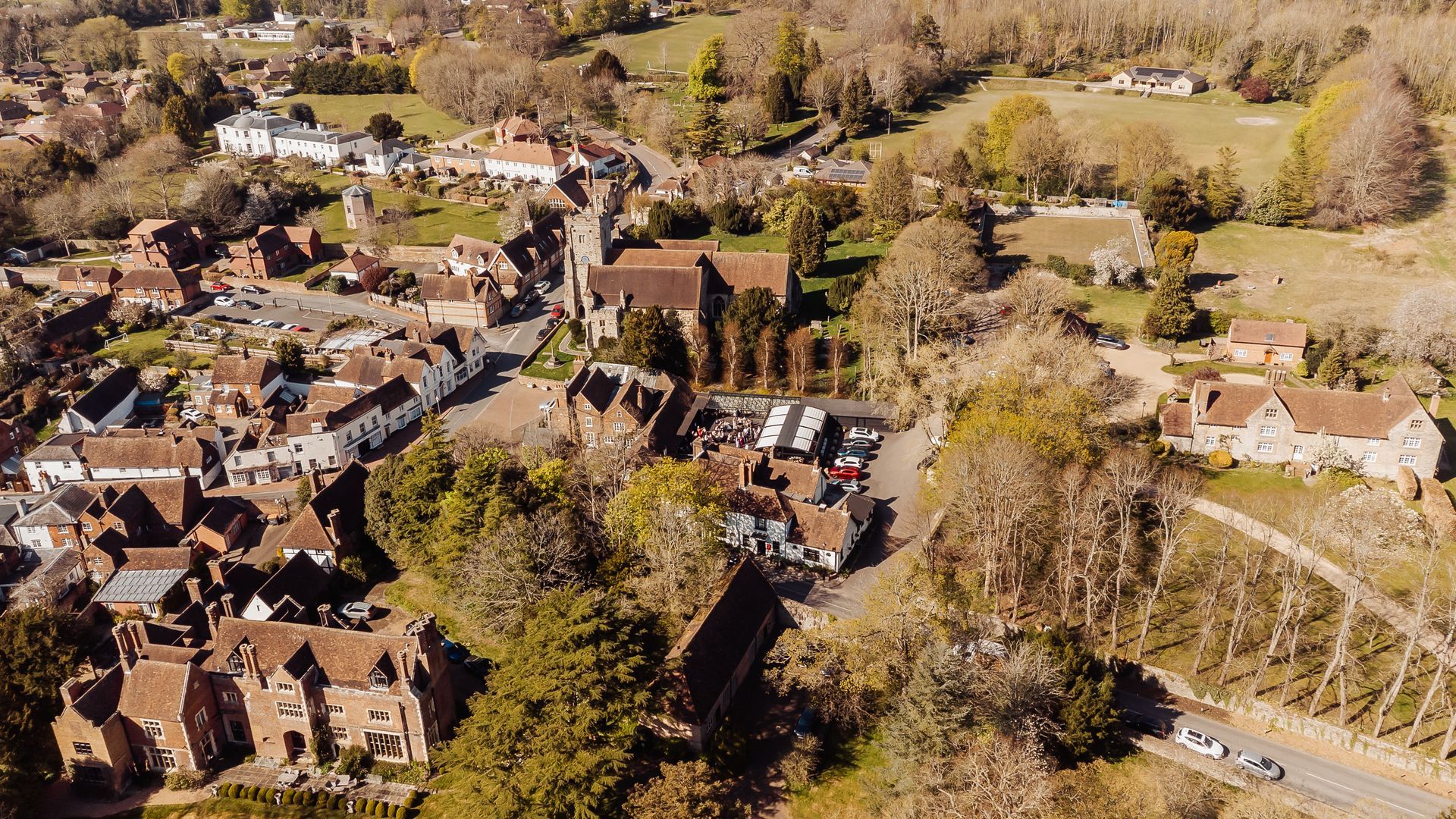 Aerial view of a small village with brick houses, trees, and open fields in autumn.