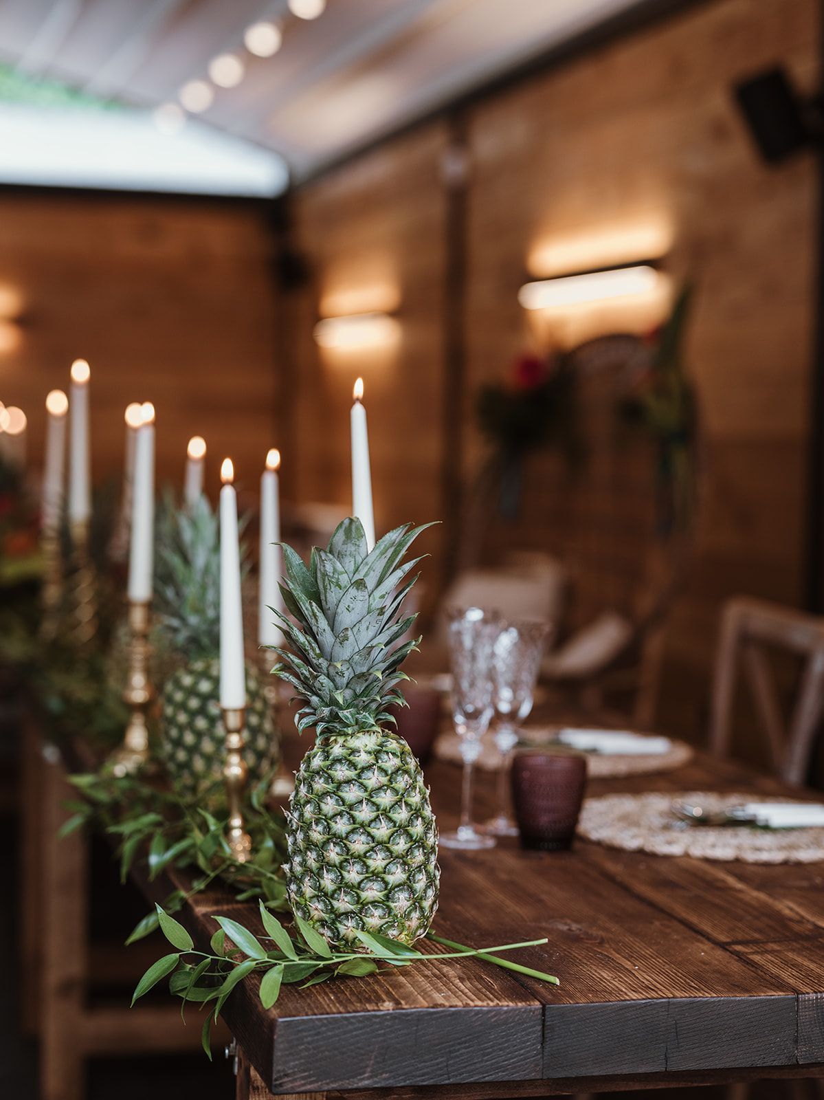 Rustic table with candles, a pineapple centerpiece, and blurred restaurant seating in the background