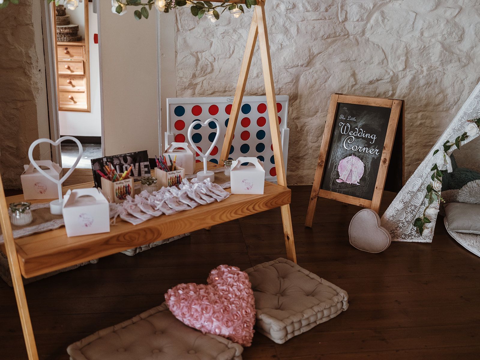 Rustic tabletop display with heart decor, pink accents, framed art, and woven cushions on a wooden floor