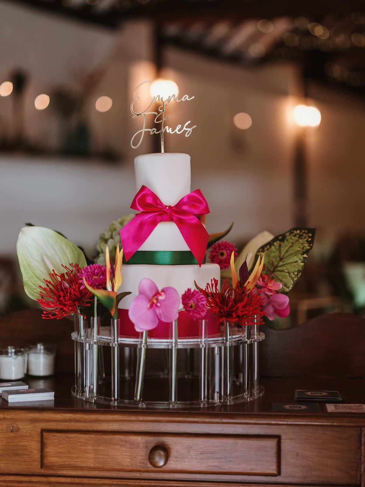 Decorated white cake with pink bow and flowers on a glass stand on a wooden table
