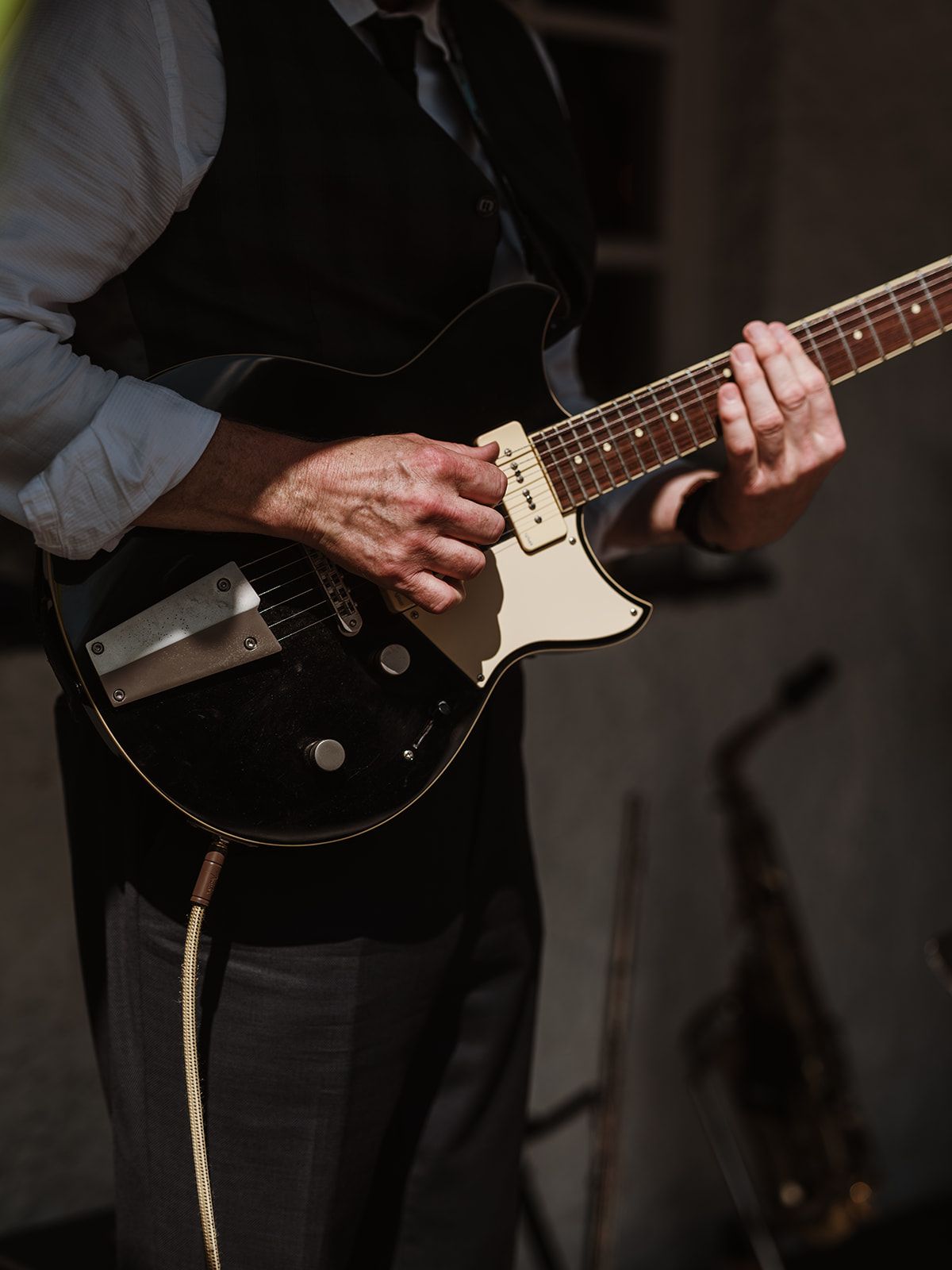 Person playing a black electric guitar on stage under dim lighting