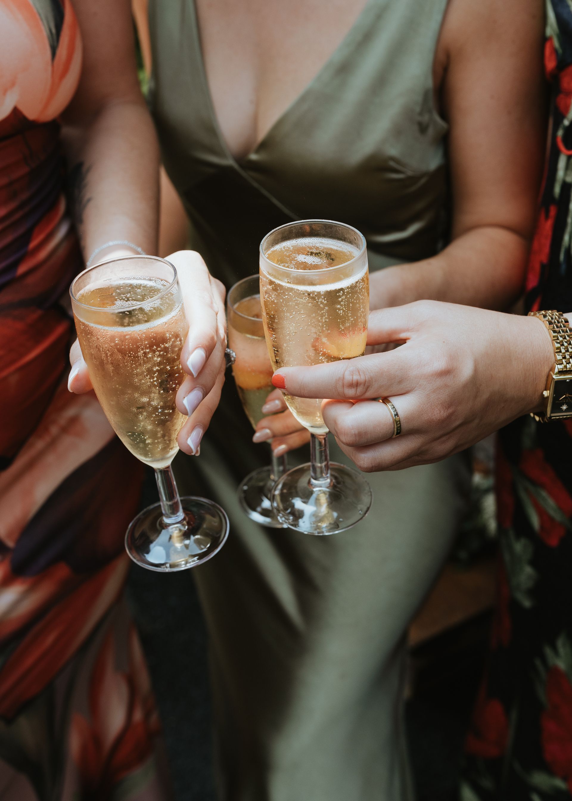 Two people in green outfits clink champagne flutes filled with sparkling wine at a celebration.