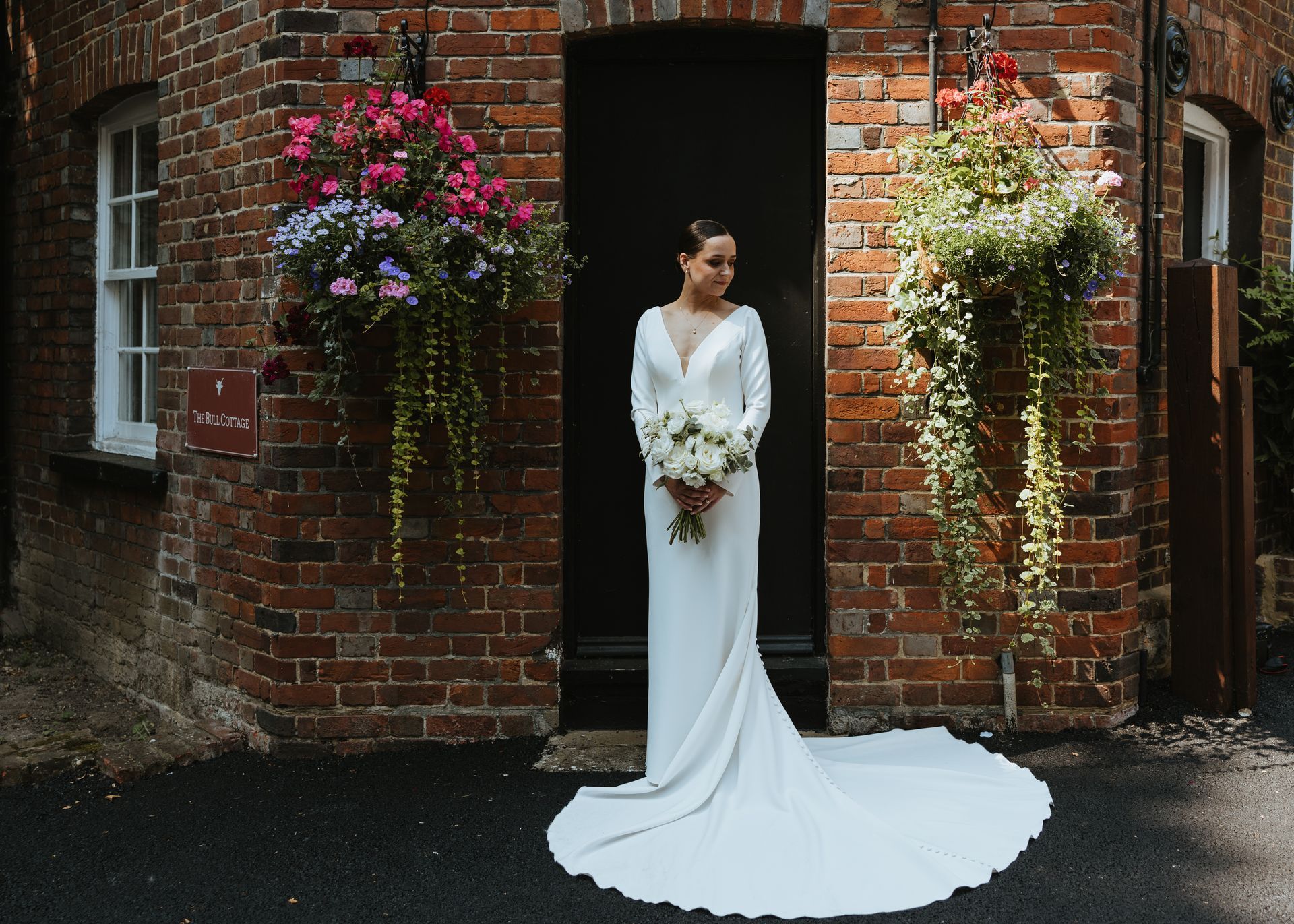 Woman in a white wedding dress standing in a brick doorway with hanging flowers