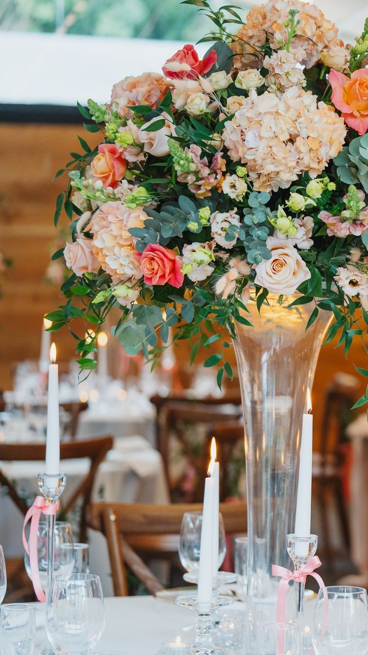 Tall floral centerpiece with pastel pink, peach, and red flowers on a decorated dining table