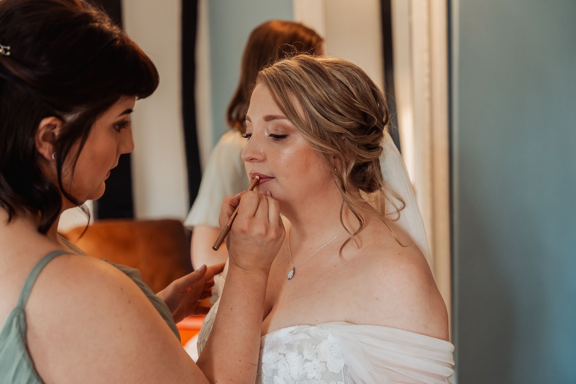 Bride getting makeup applied by a stylist in a softly lit room