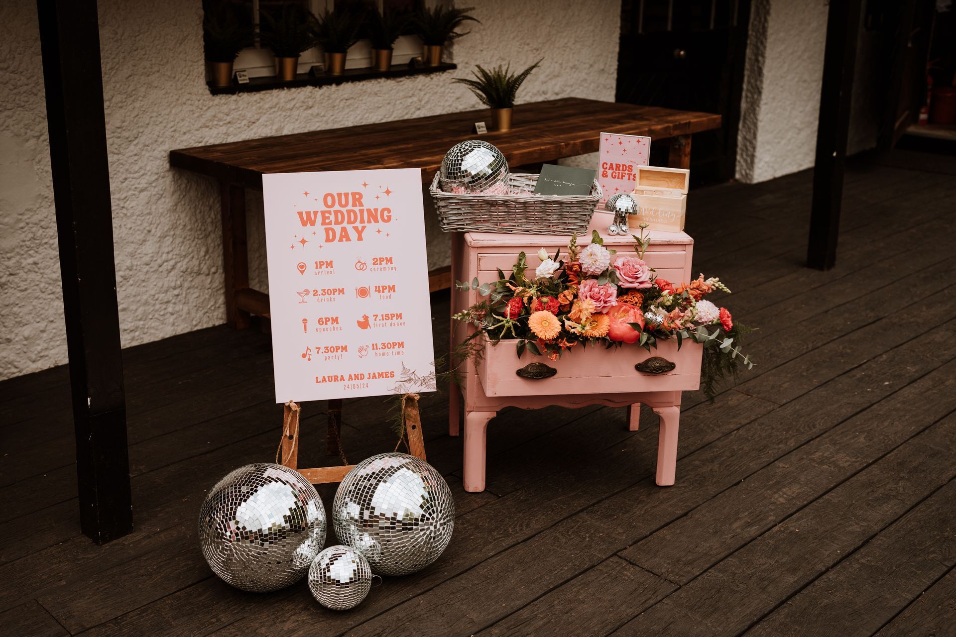 Wedding welcome display with pink flowers, silver balloons, and a sign on a dark wooden porch