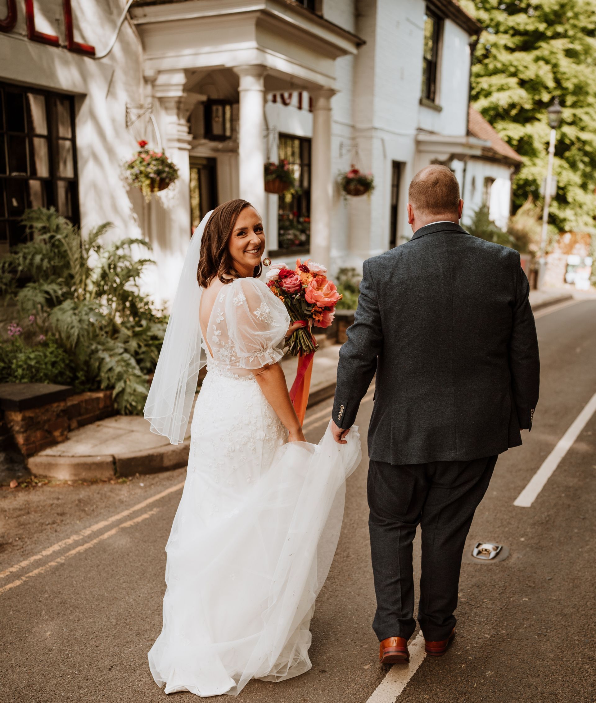Bride and groom walking away on a rainy street, bride holding bouquet and smiling back
