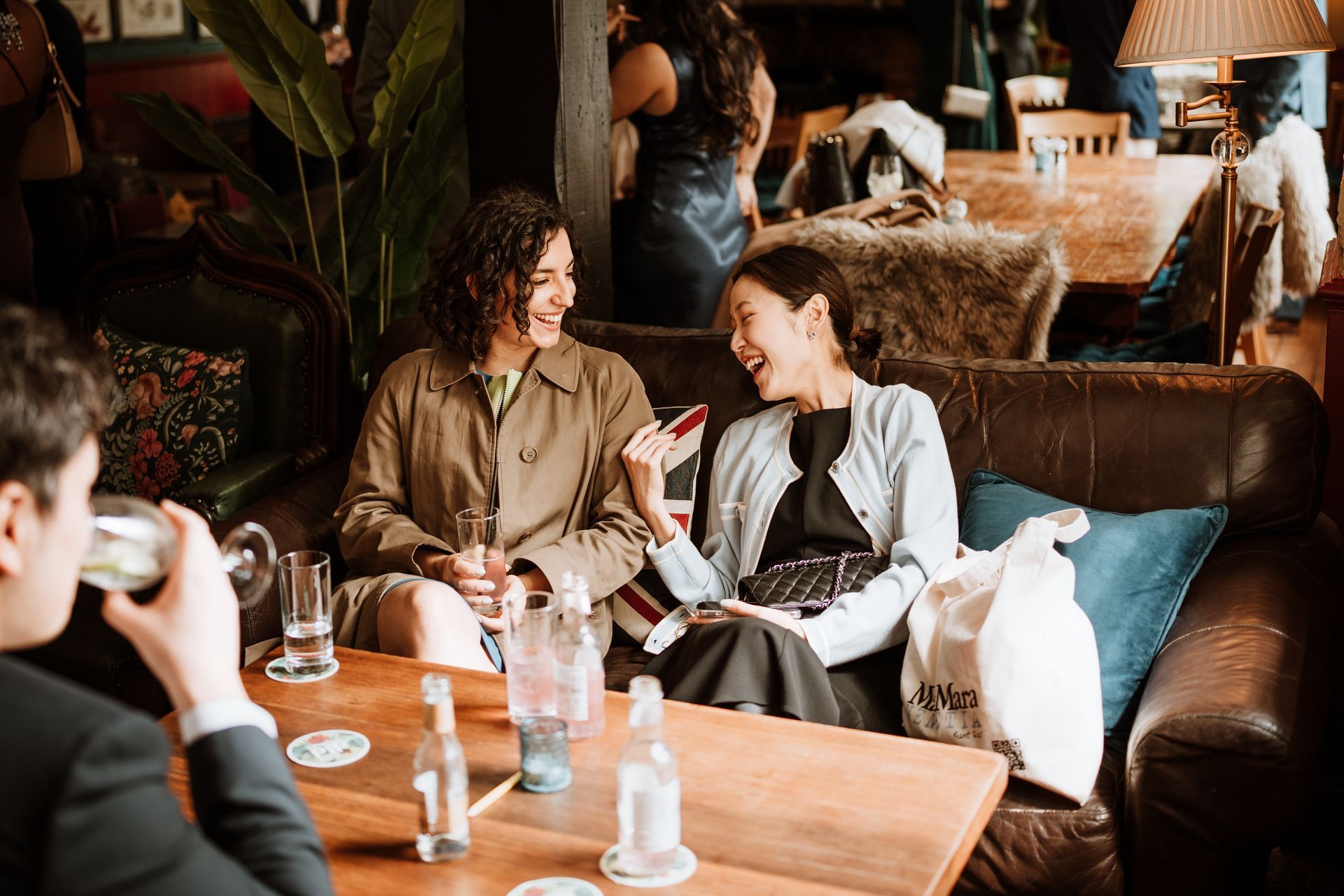 Two friends chatting on a leather couch in a cozy café, with drinks on the table.