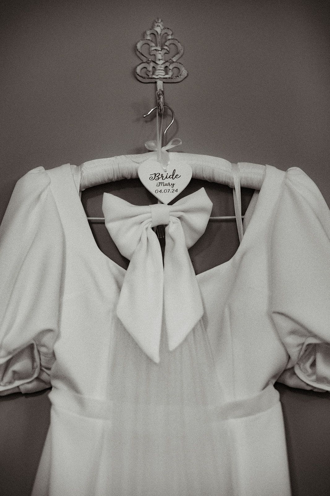 White dress with puff sleeves and bow hangs on a hanger against a wall.