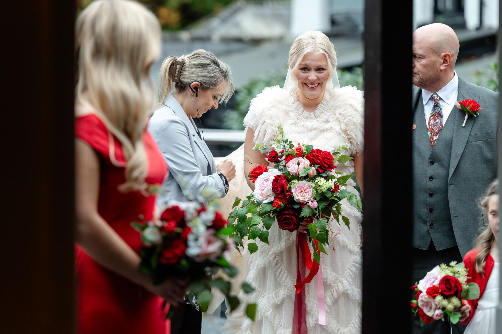 Wedding party holding red-and-white bouquets, with a bride in white at center outdoors