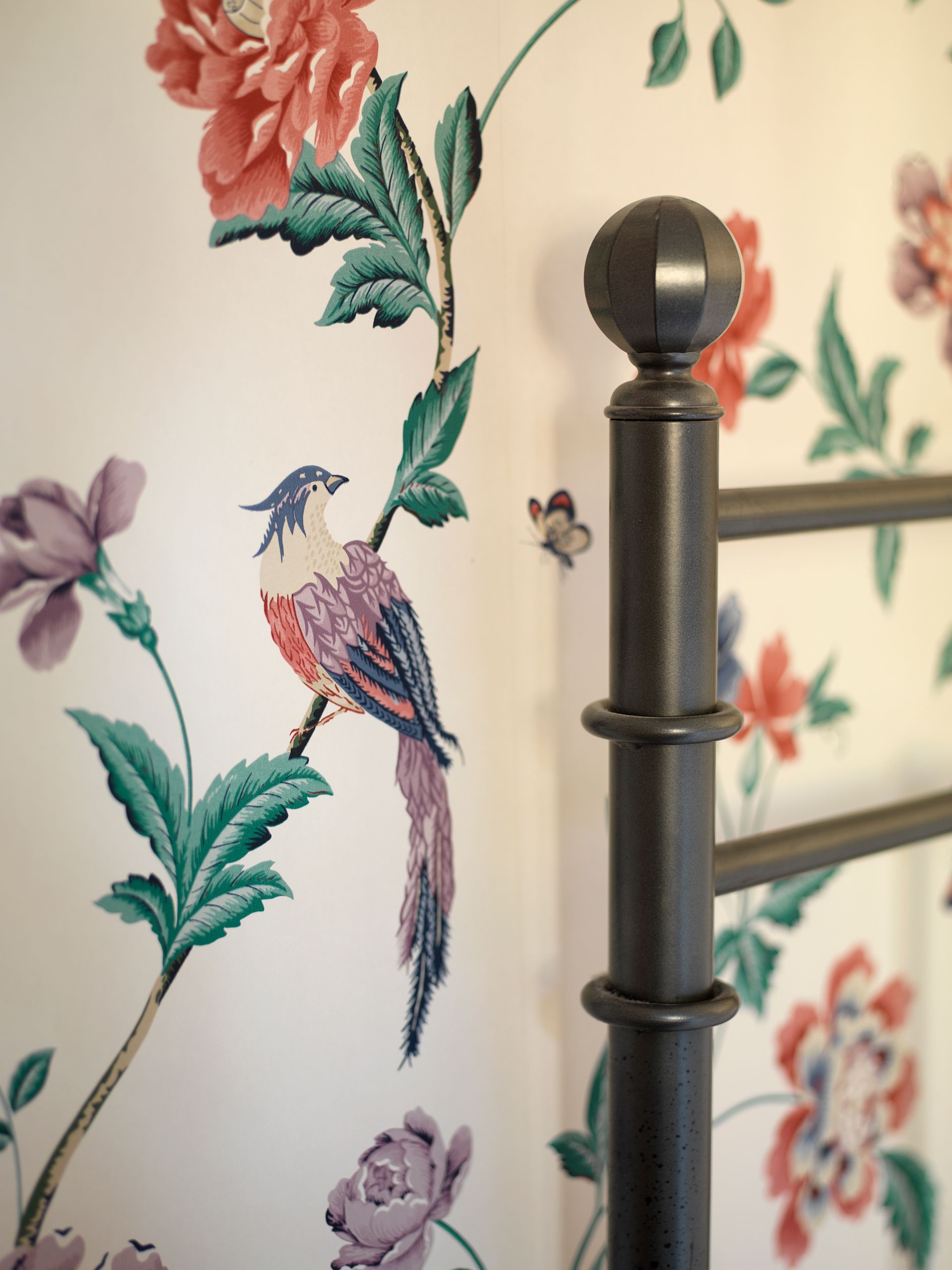 Floral wallpaper with colorful birds beside a metal bedpost and railings