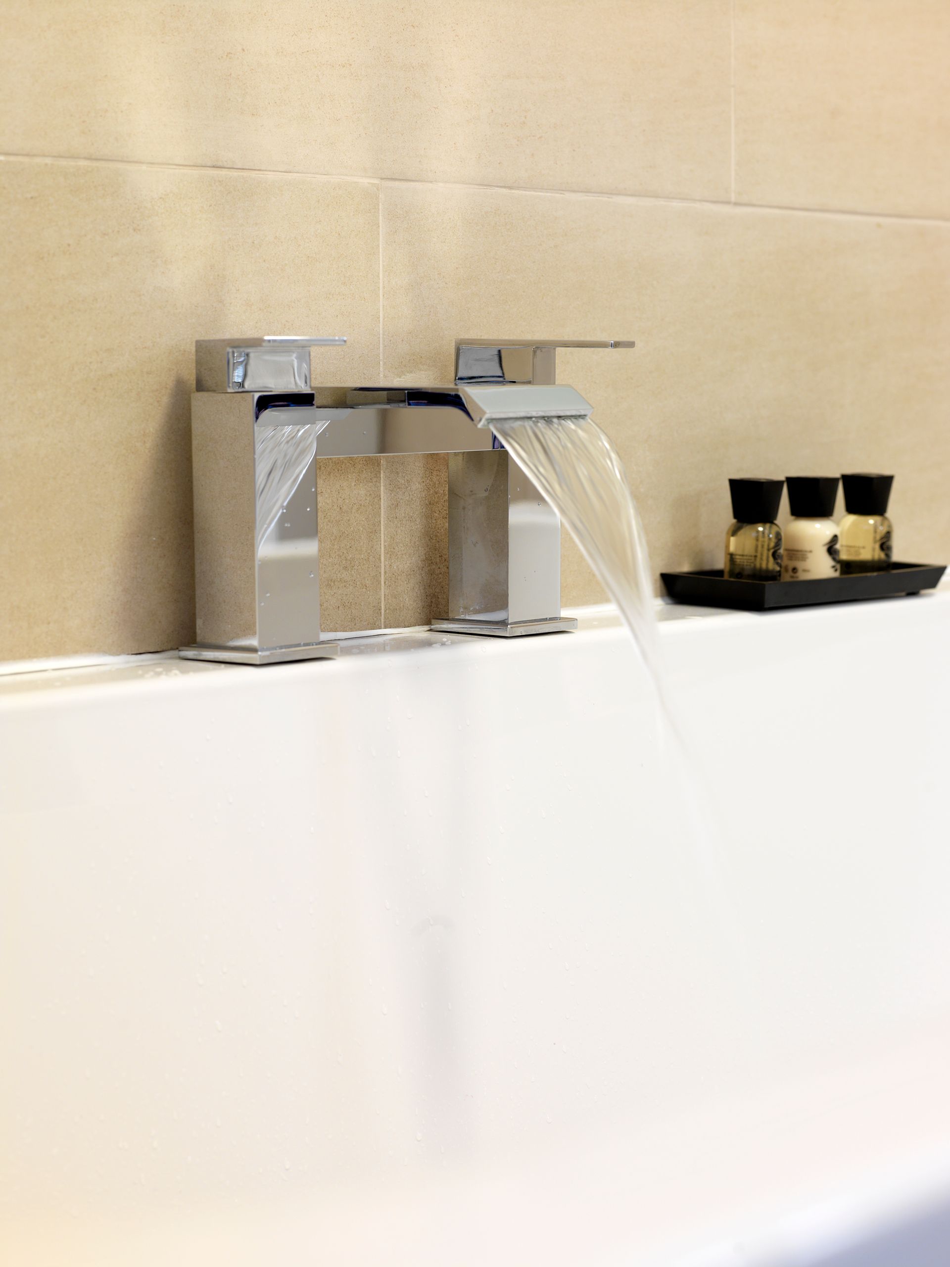 Bathroom faucet with water flowing into a white bathtub beside gold cups on a tray
