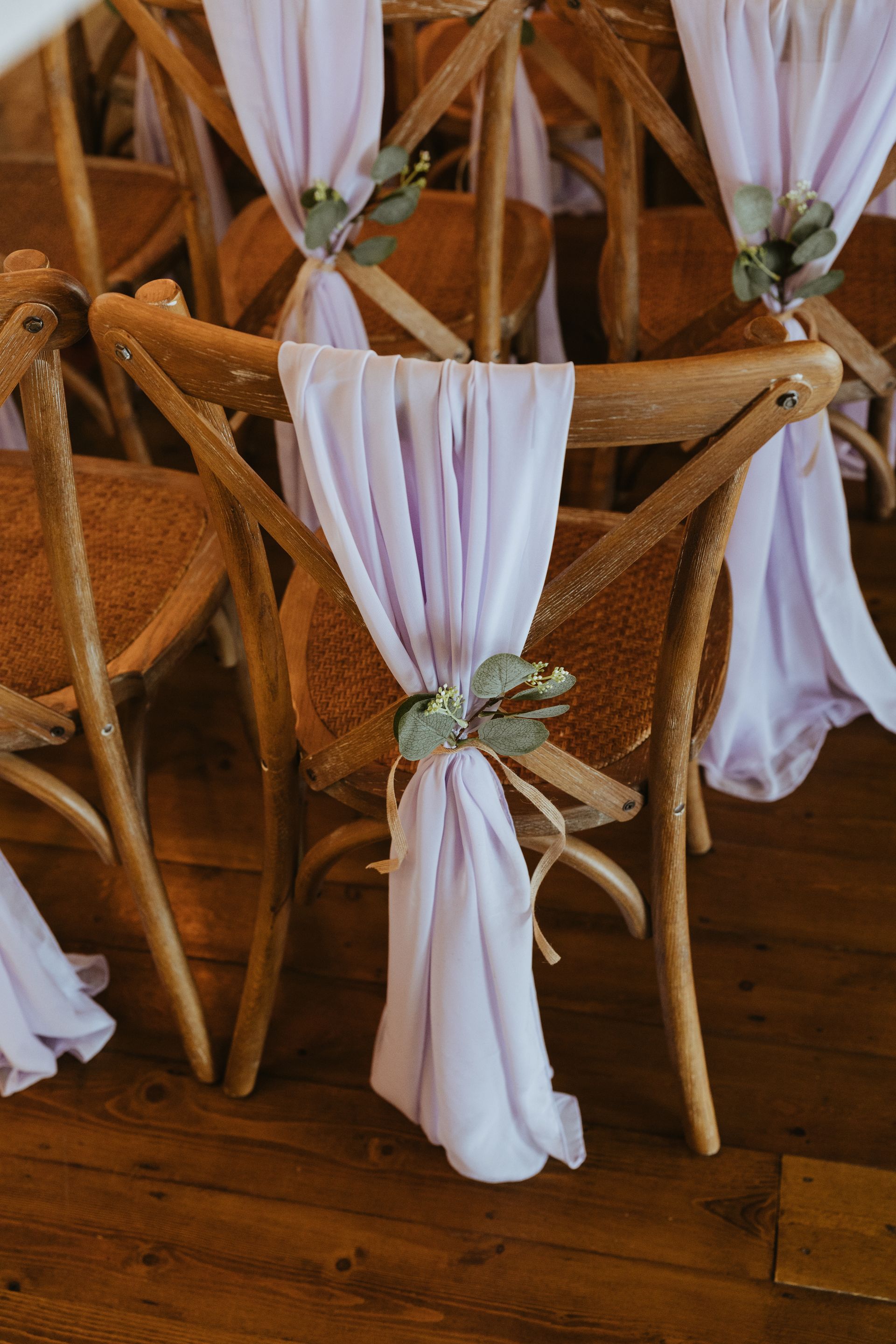 White-draped wooden chairs tied with green-and-white ribbons on a wooden floor