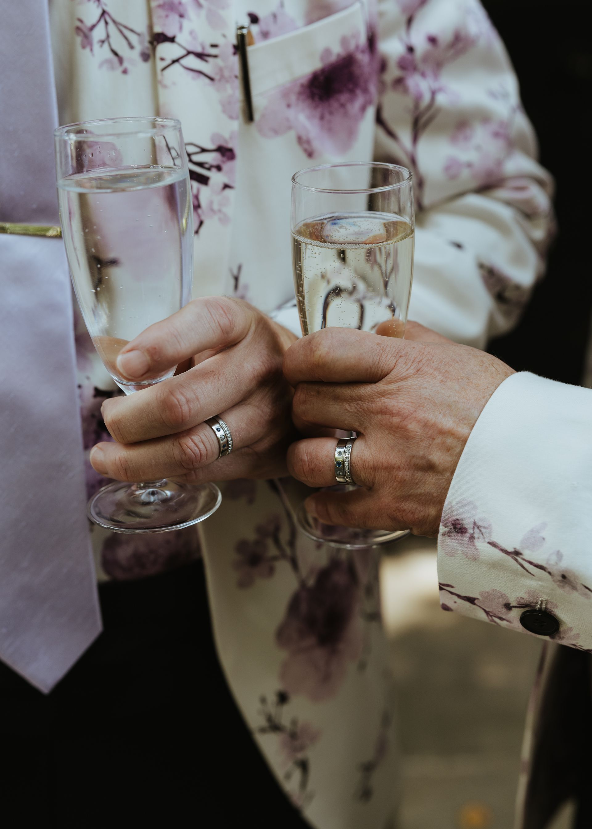 Hands in floral jackets clink champagne flutes at an indoor celebration.