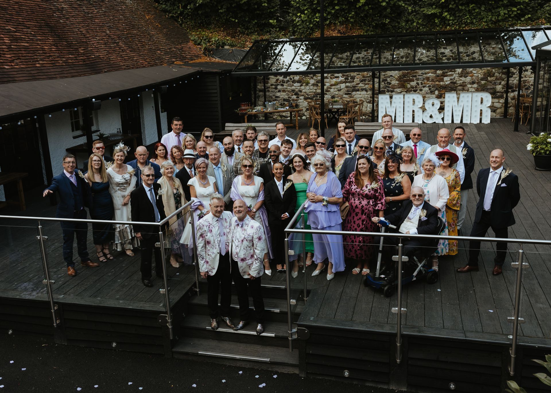 Large group posing on a deck in front of a building, with large “M&M” letters in the background