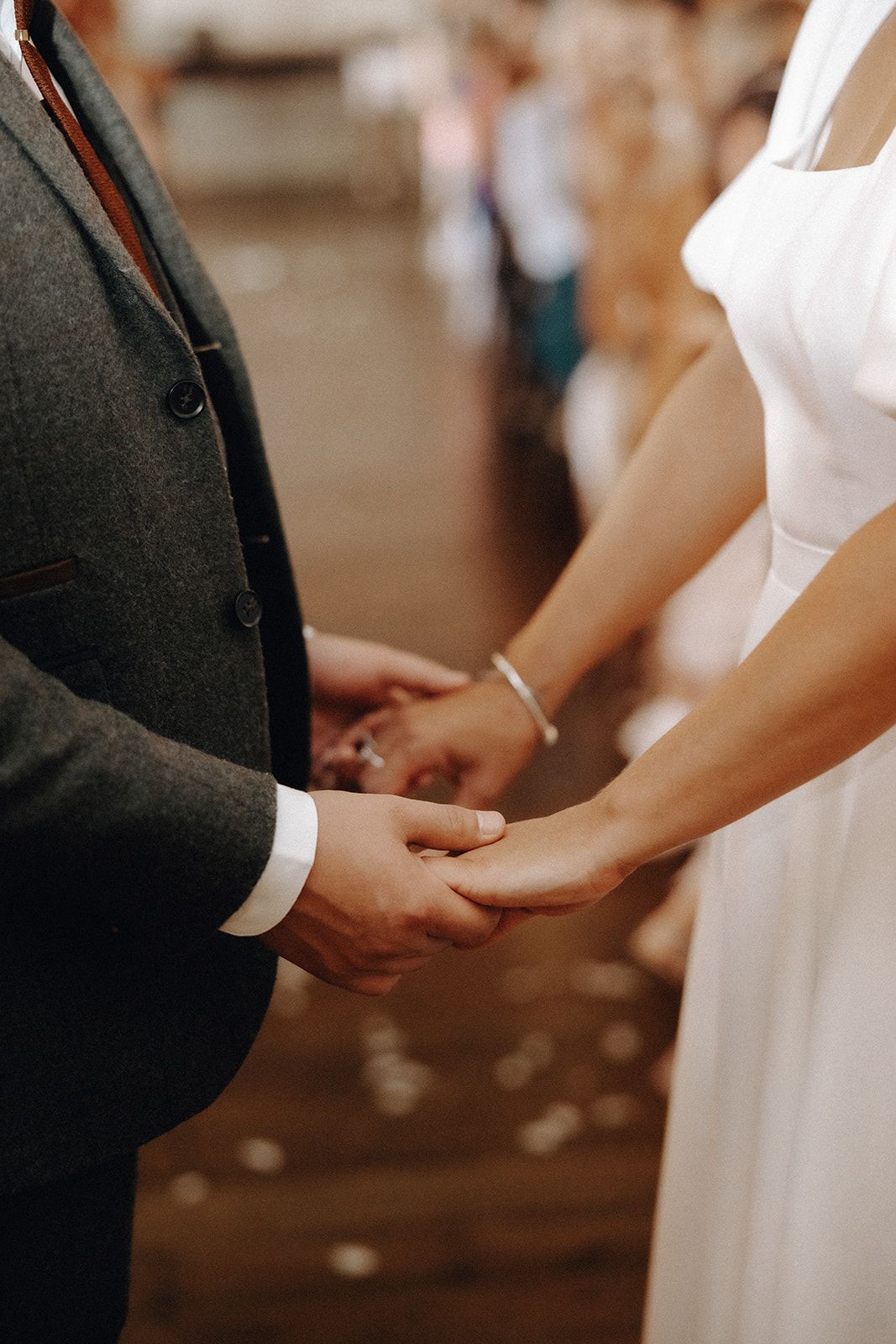 Two people holding hands at a wedding ceremony, with a black suit and white dress visible.