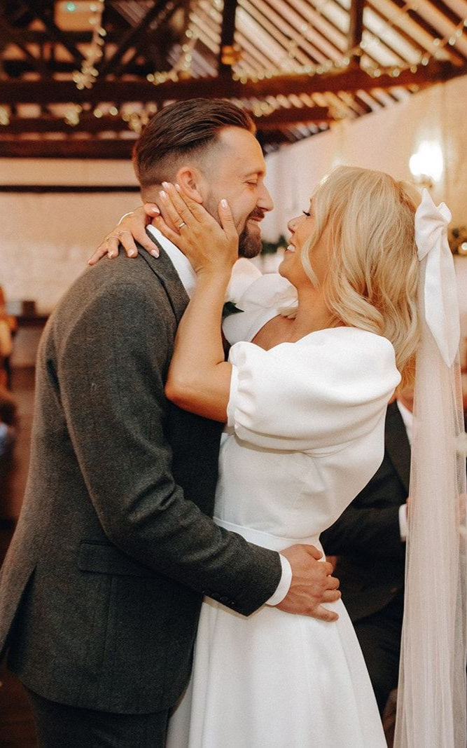 Couple embracing and kissing in a warmly lit indoor setting, dressed in black and white.