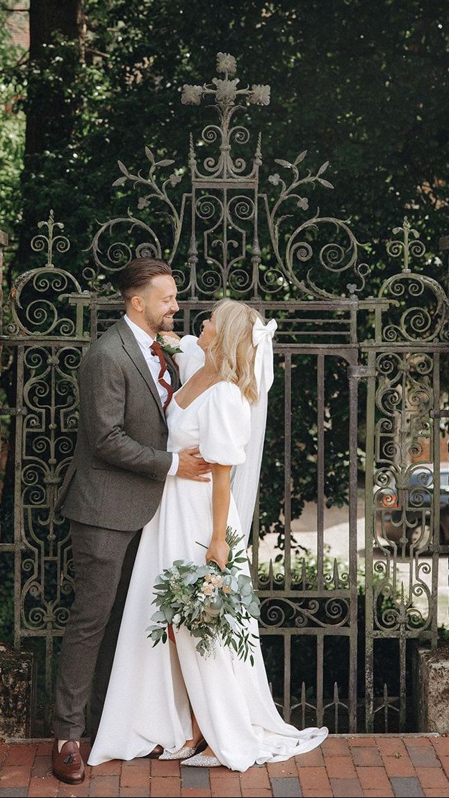 Bride and groom kissing in front of ornate wrought-iron gate, bride holding a bouquet