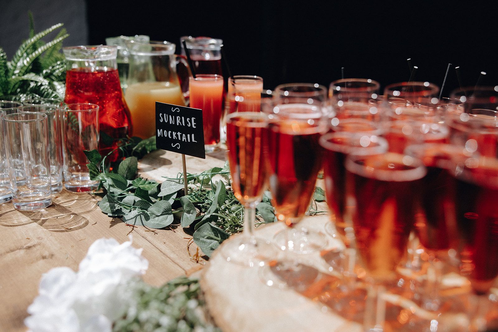 Rows of red and orange cocktails on a table with greenery and a black drink sign at a buffet display