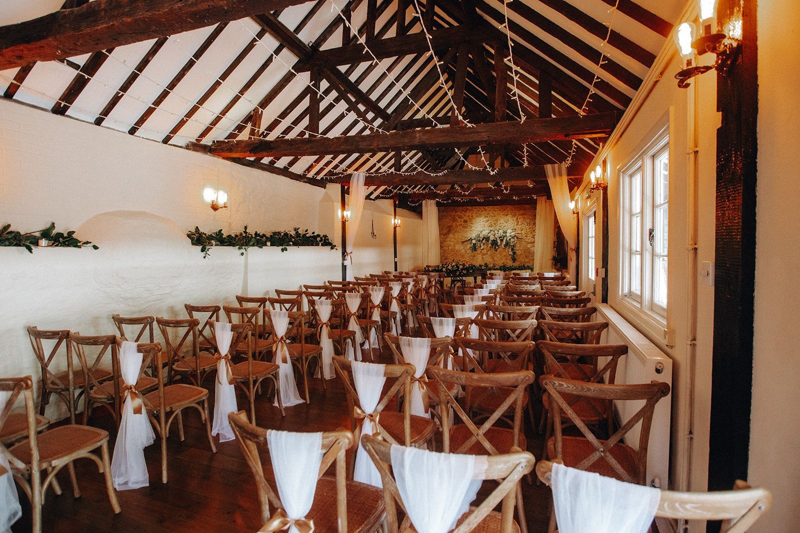 Rows of wooden chairs and tables in a rustic, warmly lit banquet hall with exposed beams