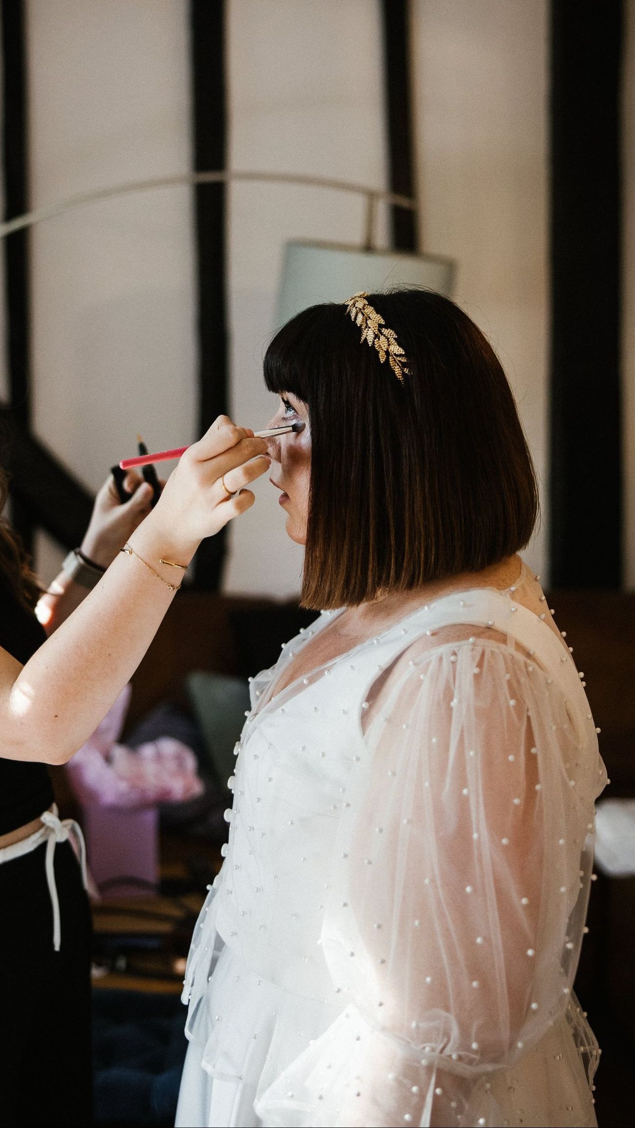 Person in a white dress having makeup applied before a ceremony