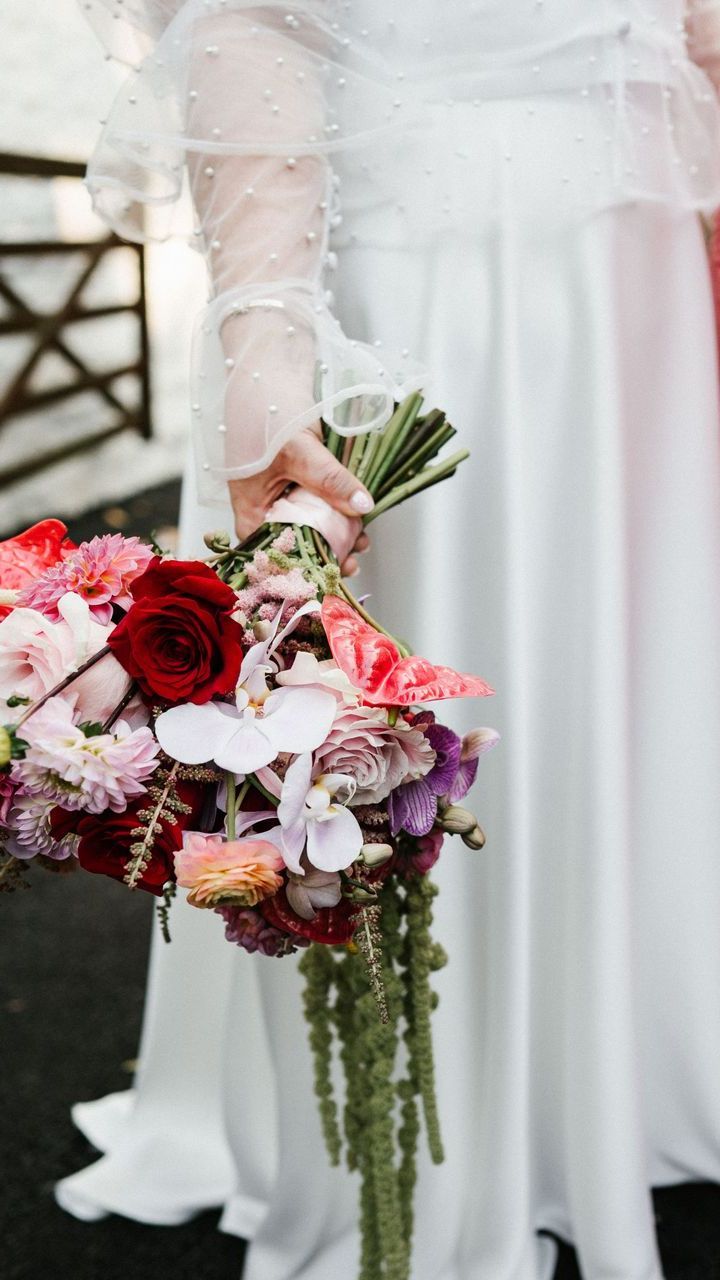 Bride holding a cascading bouquet of red, pink, and white flowers with greenery