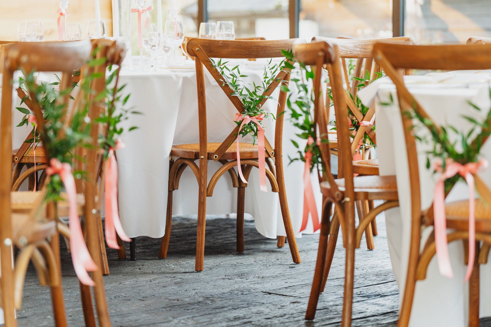 Decorated wooden chairs with white covers and greenery at a bright wedding reception table